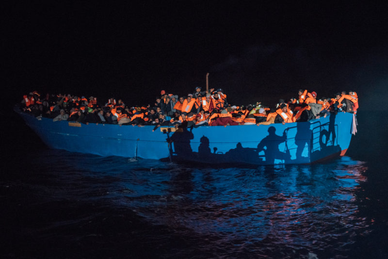 Ein stark überbesetztes Schaluchboot bei Nacht im Scheinwerferlicht
