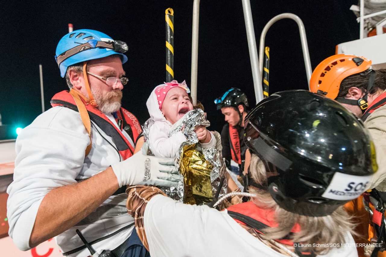An Bord der Aquarius wird ein weinendes Baby von einem Rettungsteammitglied an ein anderes übergeben