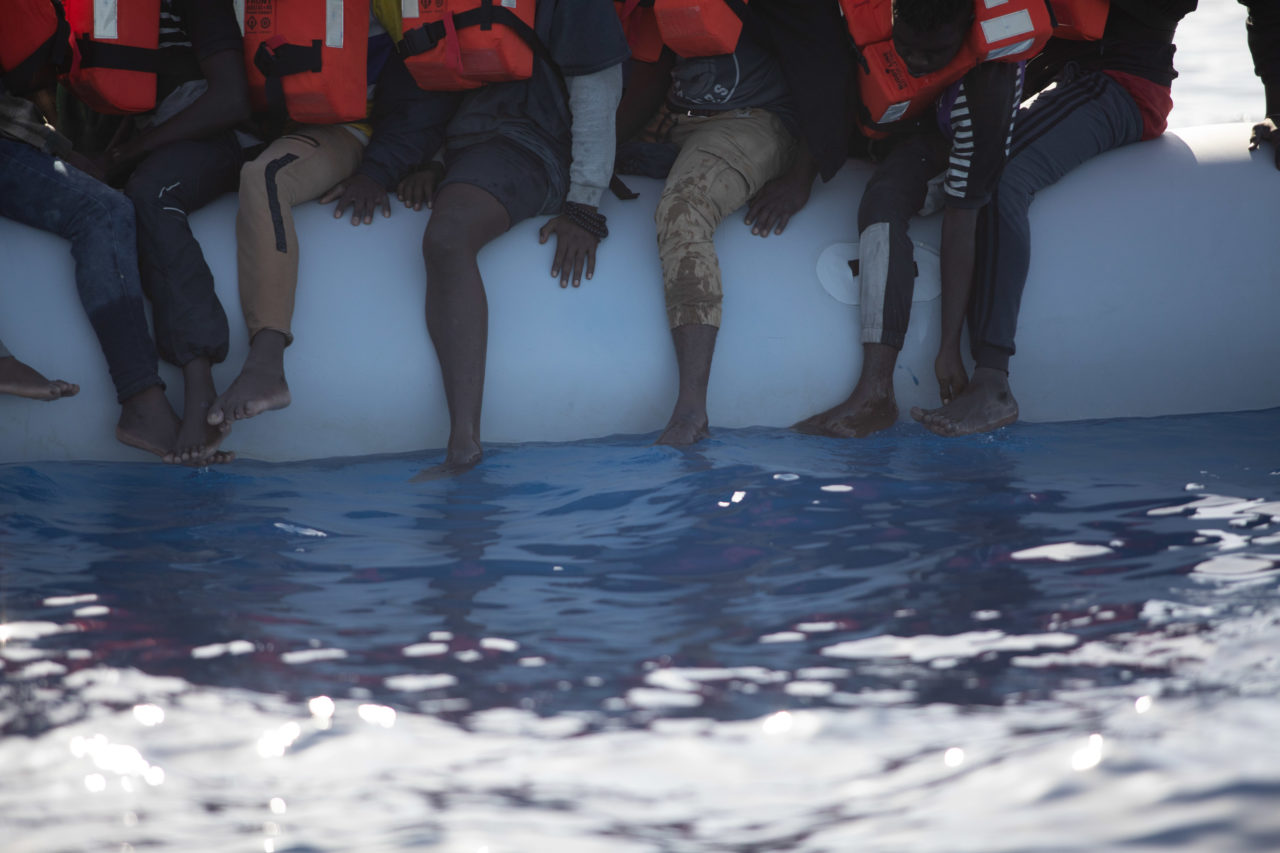 Die Beine von Menschen in einem Schlauchboot ragen über dessen Seitenwand