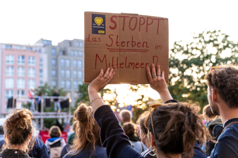 SOS Humanity mit einem Schild mit Logo (blau gelb) auf einer Demo in Berlin