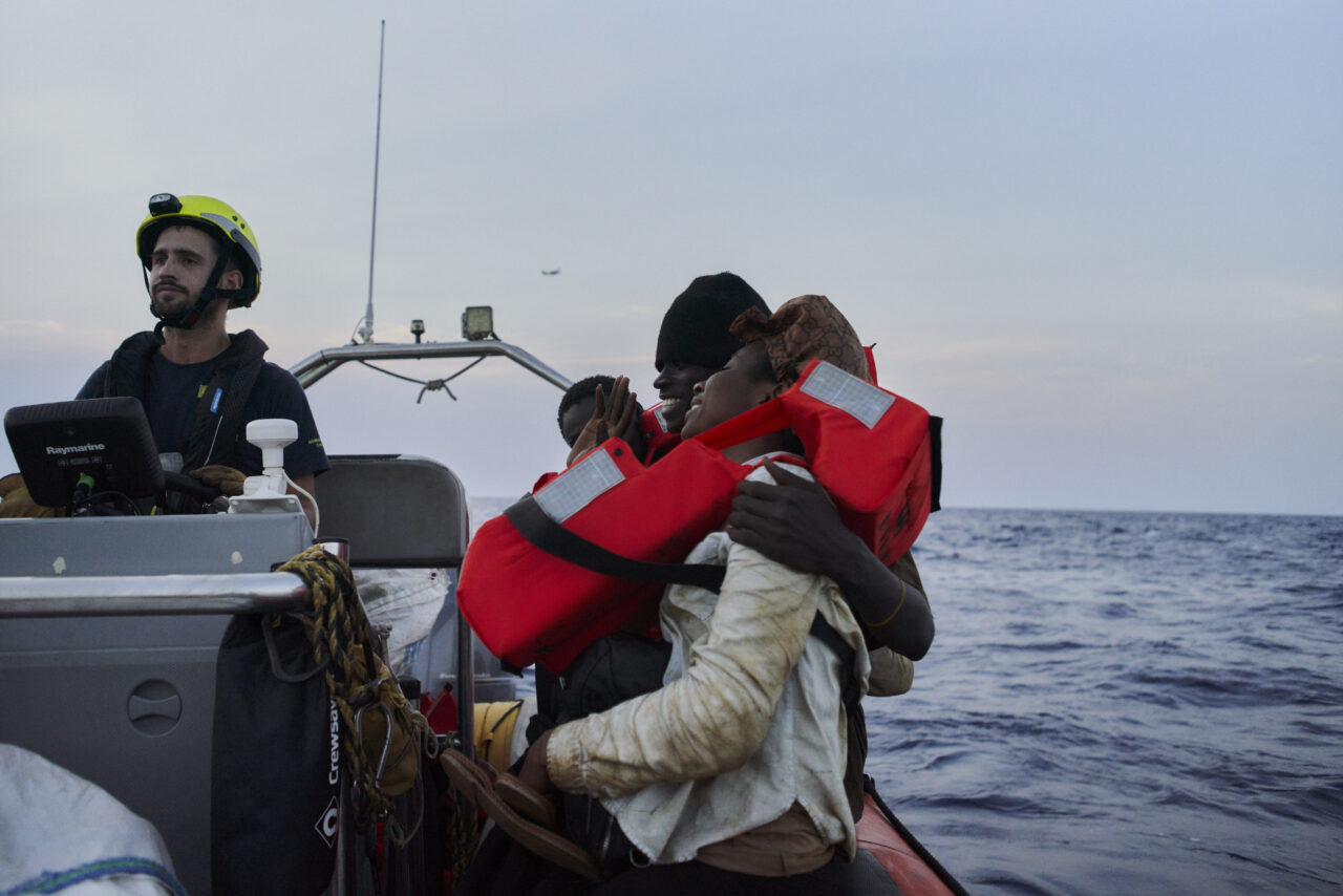 Zwei Gerettete mit orangen Rettungswesten auf dem RHIB der Humanity 1 lachend.