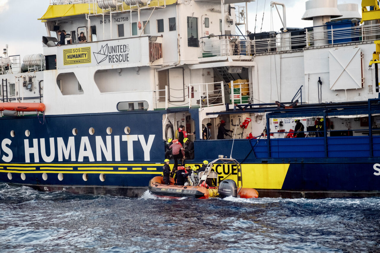 SOS Humanity im Hintergrund, im Vordergrund ein RHIB, das Gerettete an Bord bringt.