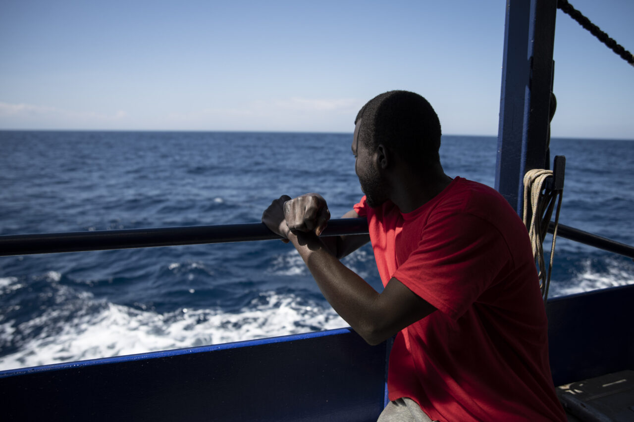 Geretteter mit rotem T-Shirt schaut von Bord der Humanity 1 auf das Mittelmeer.