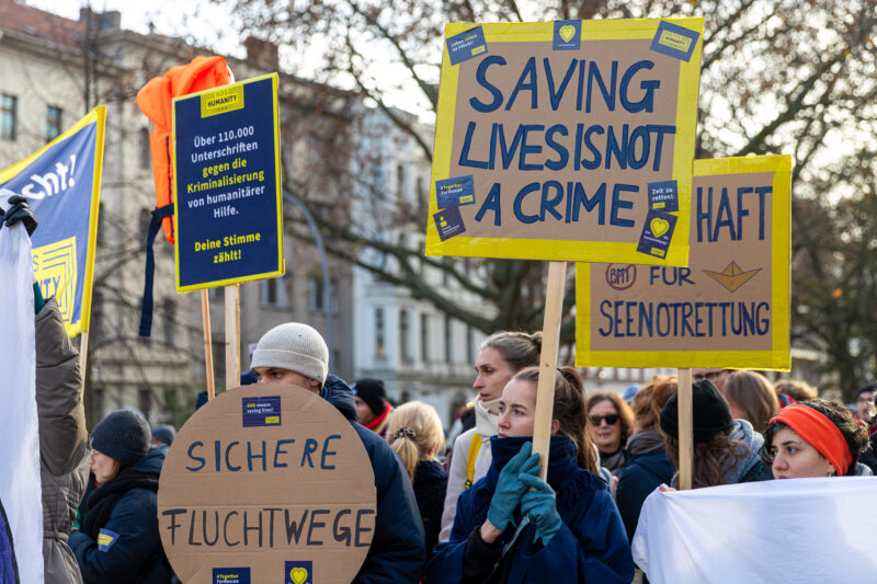 Personen auf einer Demo in Berlin mit Schildern in den SOS Humanity Farben zum Thema "Saving Lives is not a Crime".