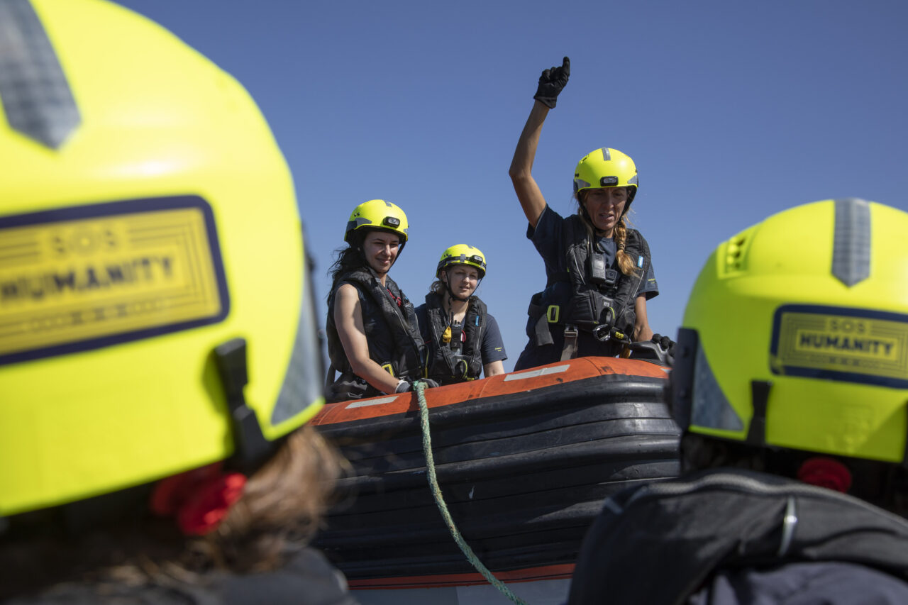 Drei weibliche Crewmitglieder - eine mit hochgestrecktem Arm - sind auf einem Schnellboot von SOS Humanity zu sehen.