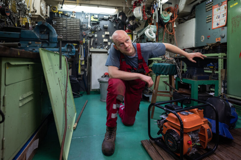 Eine Person in roter Latzhose bei der Arbeit im Maschinenraum der Humanity 1.