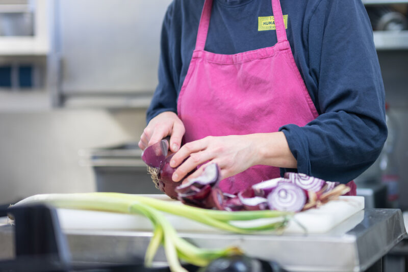 Crewmitglied mit SOS Humanity-T-Shirt und pinker Schürze schneidet Gemüse