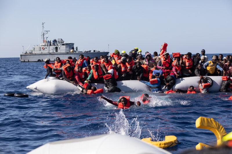 Schlauchboot mit geflüchteten Menschen, die sich teilweise schon im Wasser befinden