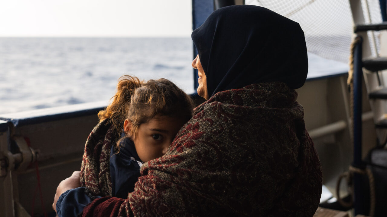 Mutter drückt ihr Kind an sich und schaut auf das Mittelmeer