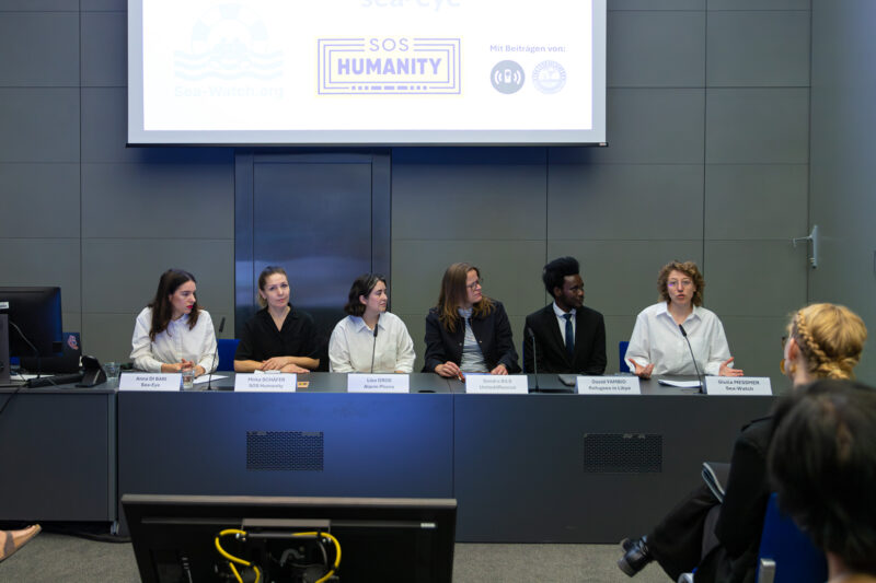 Sechs Personen vor einer Leinwand mit den Logos von Sea-Watch, Sea-Eye, SOS Humanity und United4Rescue bei einer gemeinsamen Pressekonferenz