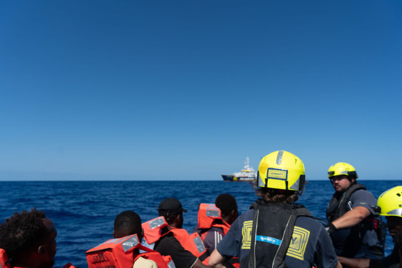 Crewmitglieder von SOS Humanity helfen Flüchtlingen, auf ihr Boot zu gelangen.