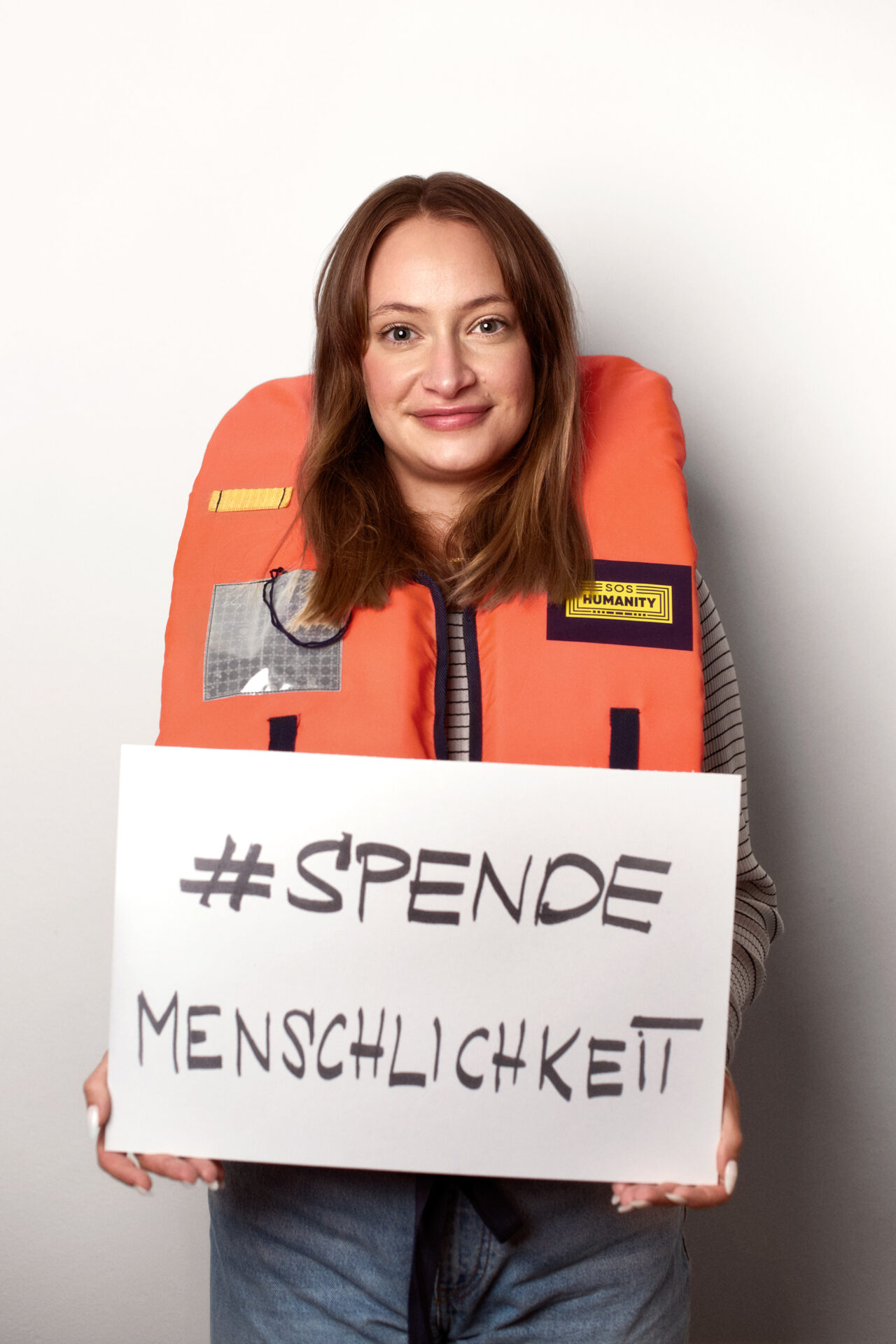 Alina Kuhl mit einer Rettungsweste und dem Schild 'SPENDEMENSCHLICHKEIT