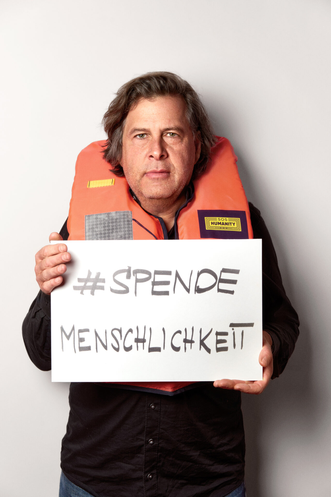 Hans-Jochen Wagner mit einer Rettungsweste und dem Schild 'SPENDEMENSCHLICHKEIT
