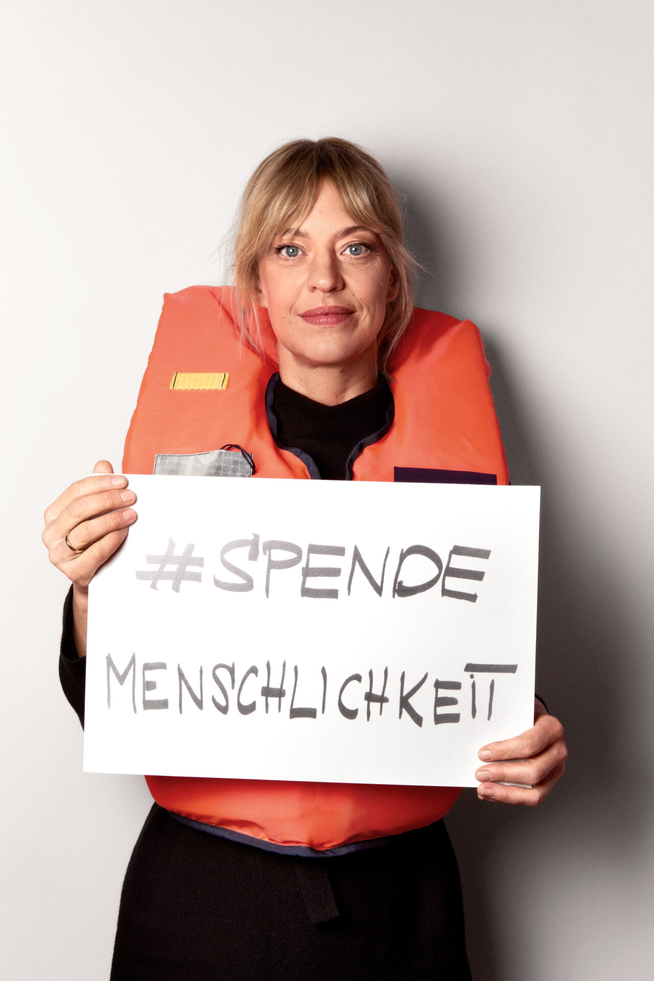 Heike Makatsch mit einer Rettungsweste und dem Schild 'SPENDEMENSCHLICHKEIT