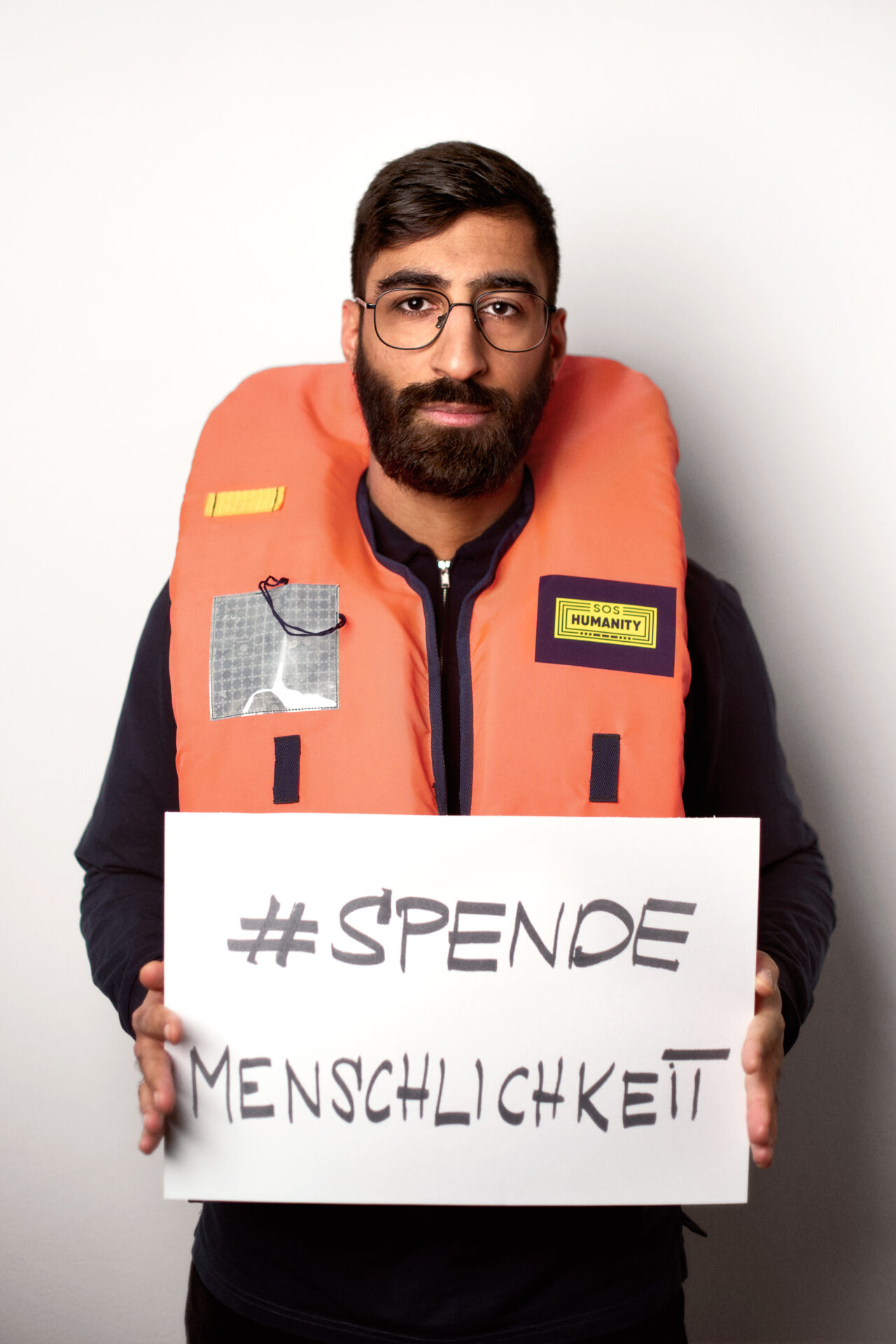 Kawus Kalantar mit einer Rettungsweste und dem Schild 'SPENDEMENSCHLICHKEIT