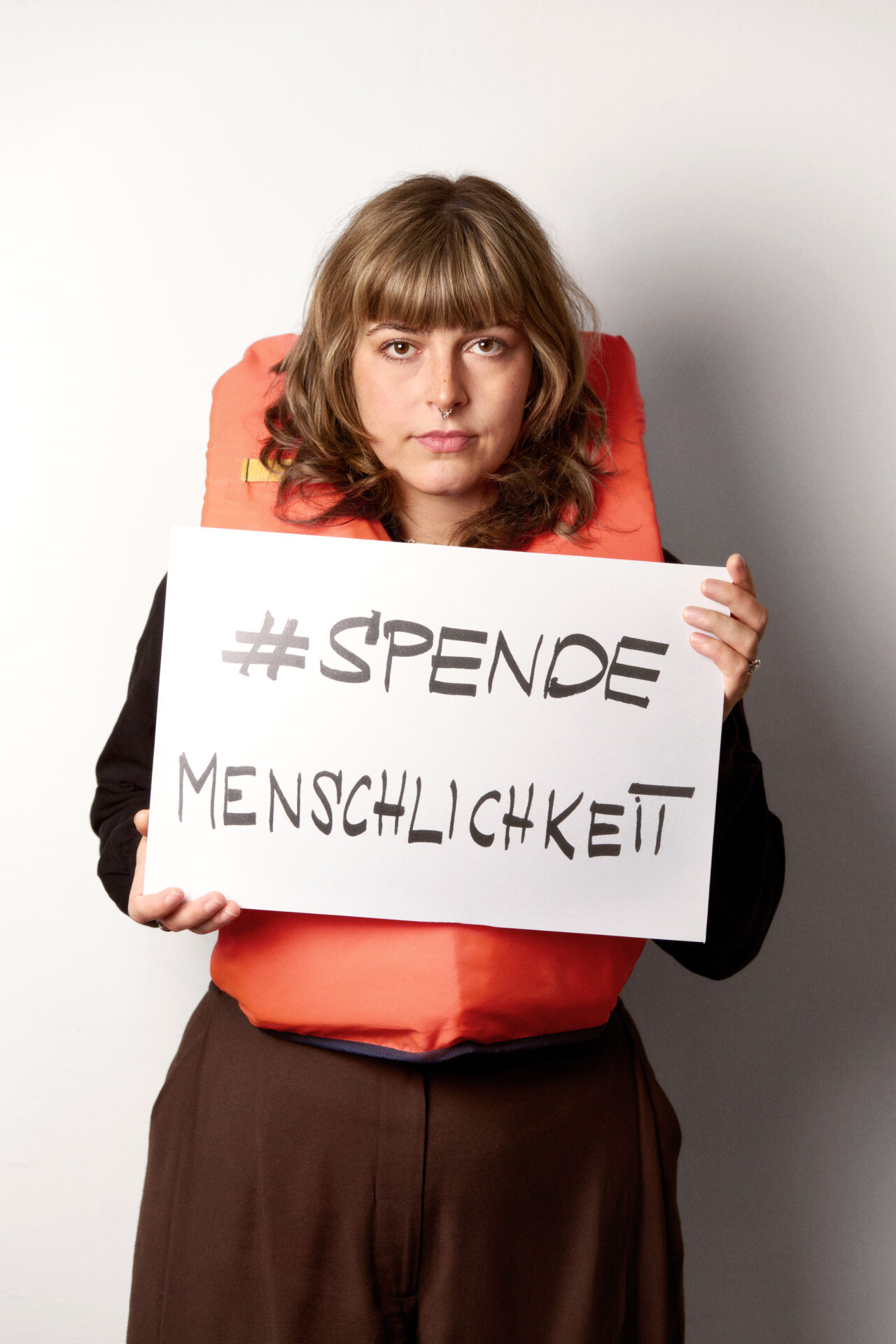 SOFFIE mit einer Rettungsweste und dem Schild 'SPENDEMENSCHLICHKEIT