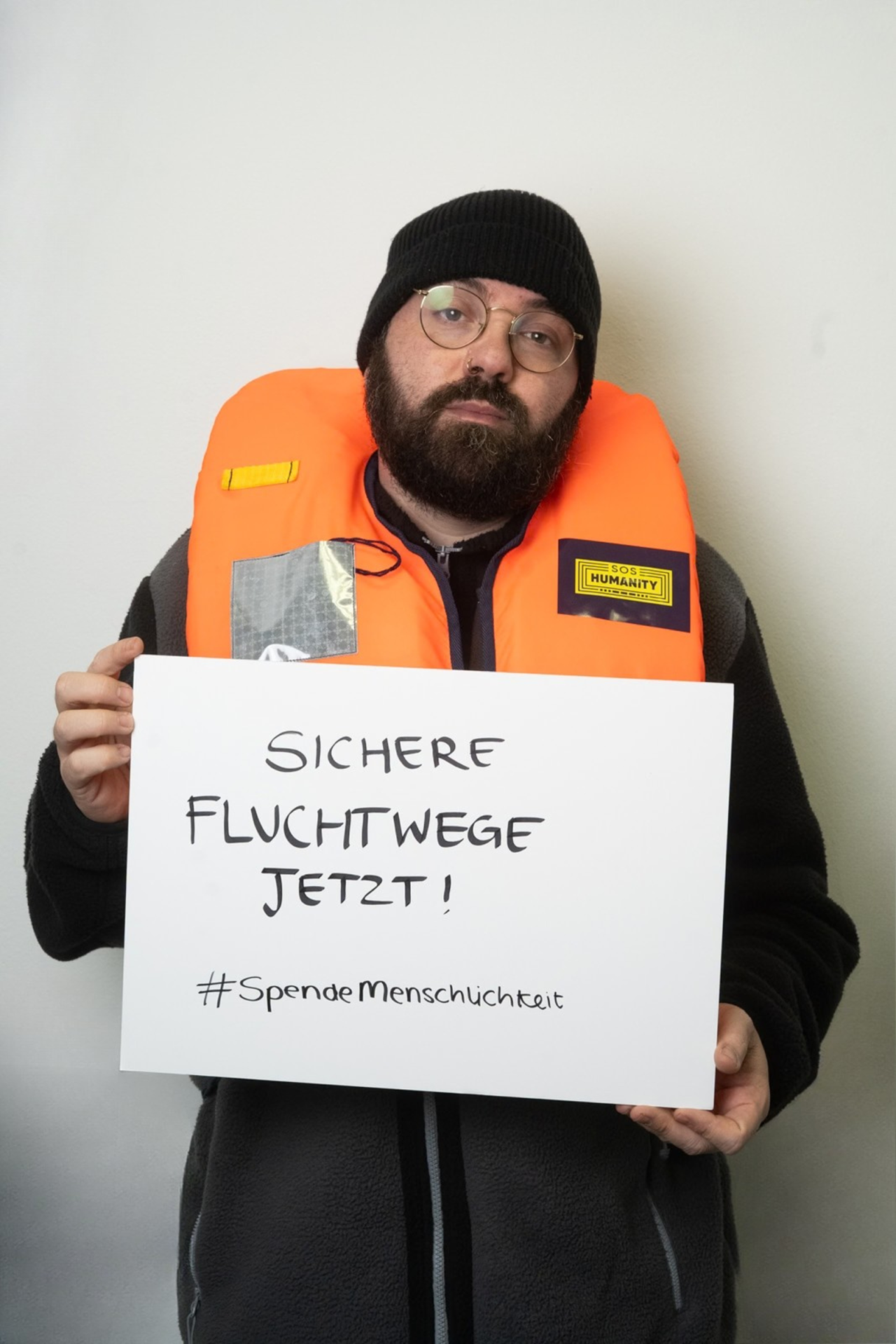 Foto von Markus, dem Sozialarbeiter, mit Schild in der Hand auf dem steht "Sichere Fluchtwege jetzt!".