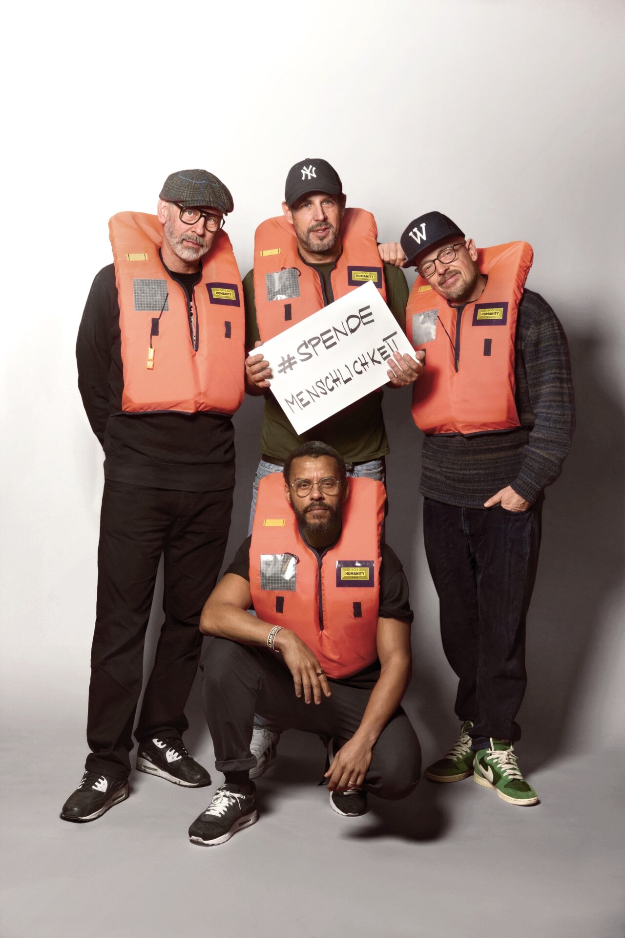 Die Band "Die Beginner" halten gemeinsam ein Schild, auf dem steht "Spende Menschlichkeit".