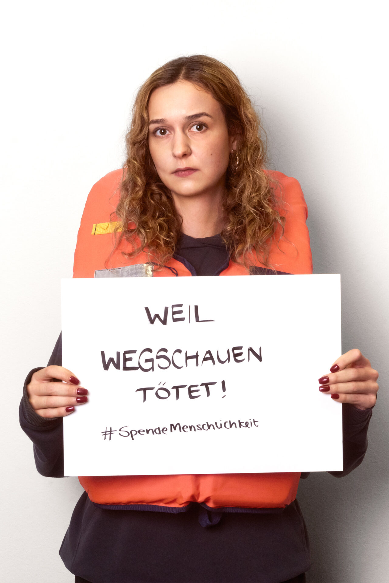 Foto von Anna, der Sozialarbeiterin mit Schild in der Hand auf dem steht "Spende Menschlichkeit!".