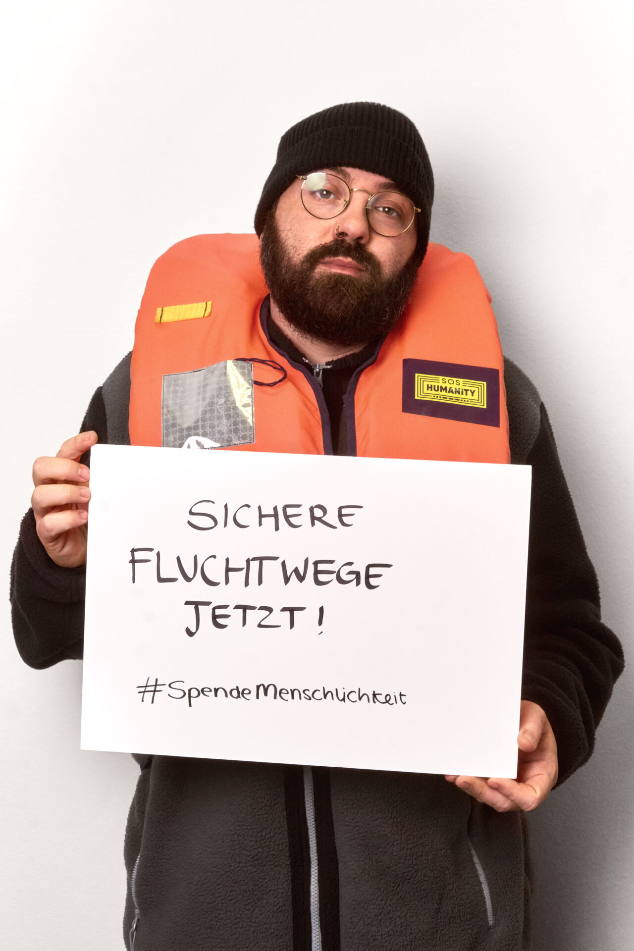 Foto von Markus, dem Sozialarbeiter, mit Schild in der Hand auf dem steht "Sichere Fluchtwege jetzt!".